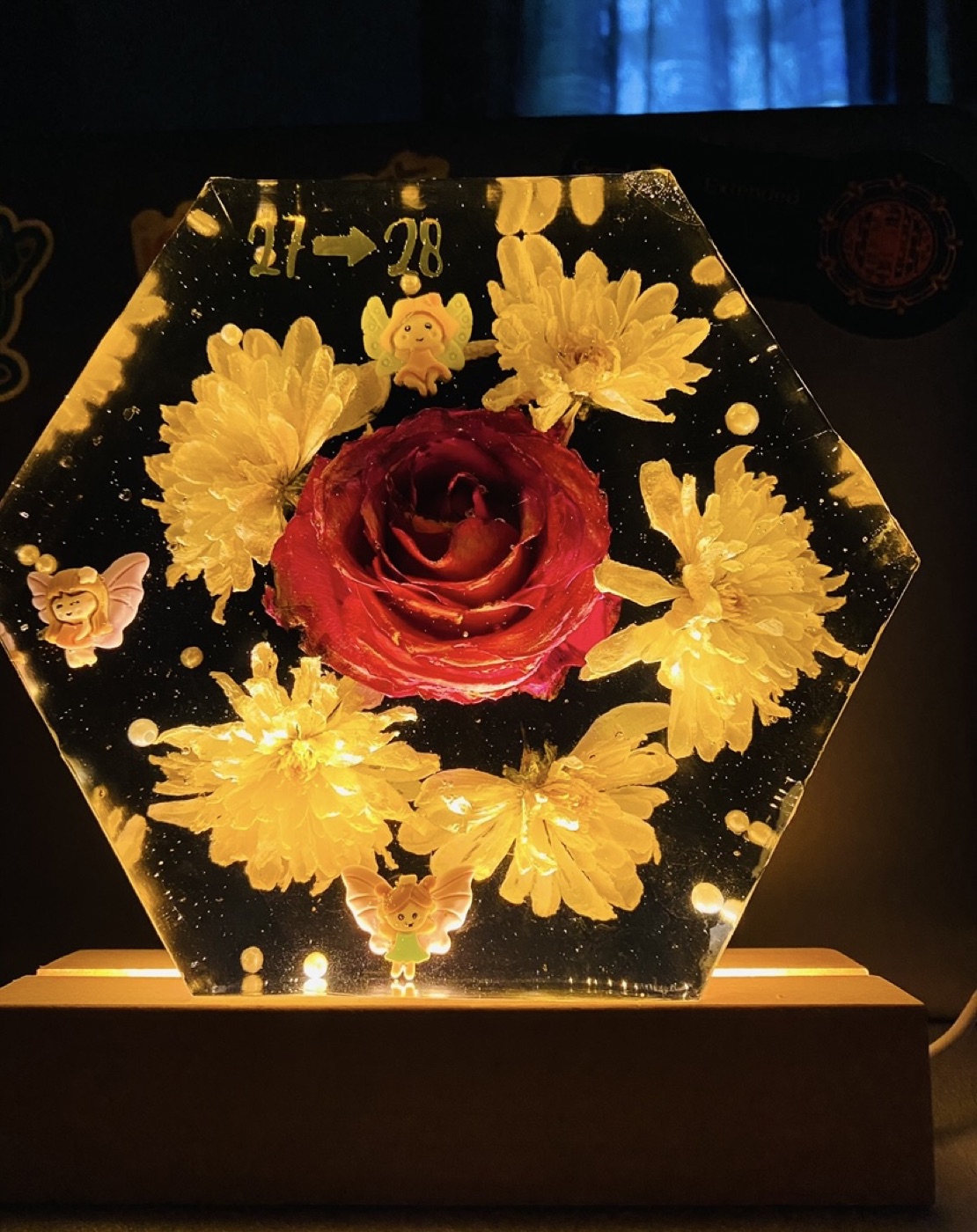 A glowing hexagonal resin lamp with a preserved rose and daisies, marking a 27th to 28th birthday